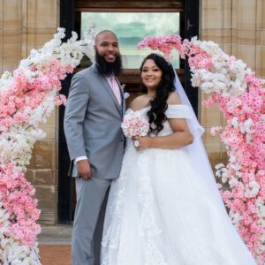 a bride and groom pose for a photo in front of a floral arch