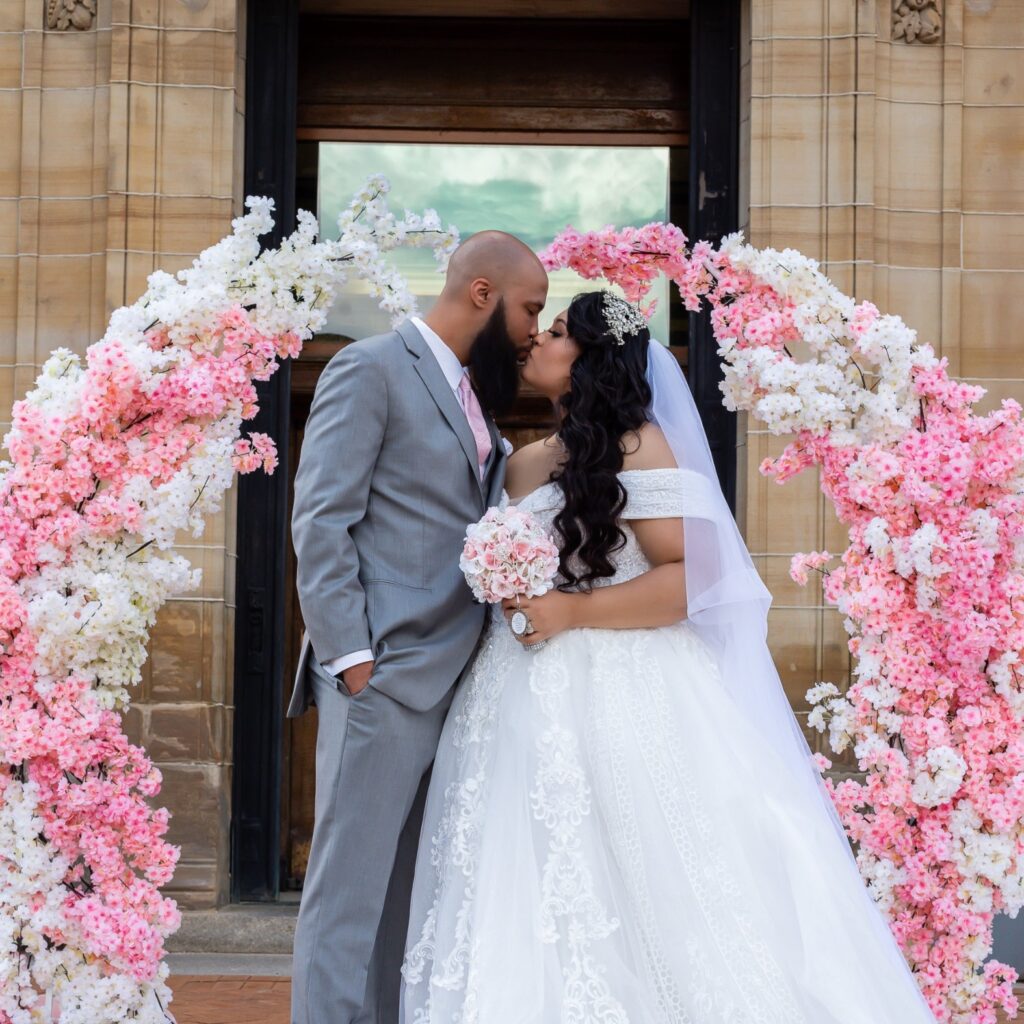 a bride and groom kissing in front of a floral arch budget wedding