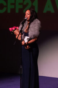 a woman standing at a microphone with flowers in her hand