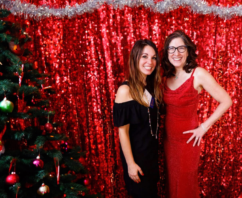 two women standing next to each other in front of a christmas tree