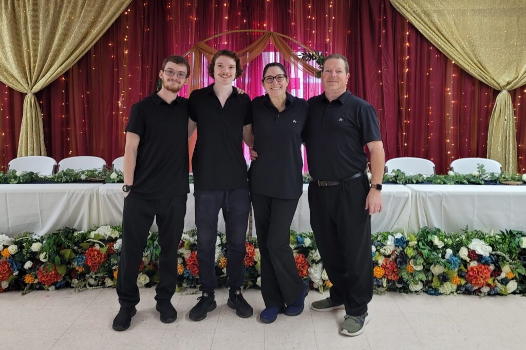 three men and a woman standing in front of a table