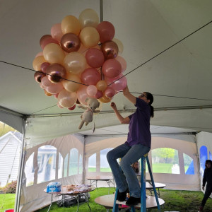 a woman on a ladder holding a bunch of balloons