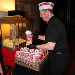 a man holding a tray of popcorn in front of a popcorn machine