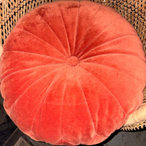 a red round pillow sitting on top of a wicker chair