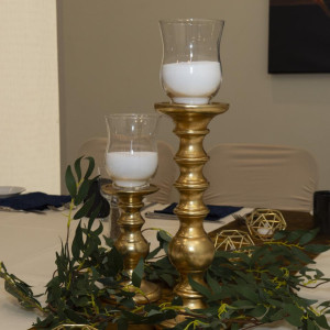 Elegant gold candlesticks styled on a formal wedding reception table with soft candlelight glow